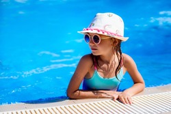 Happy girl in Sunglasses and hat in outdoor swimming pool of luxury resort on summer vacation. Healthy outdoor sport activity for children. Kids beach fun