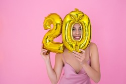 Smiling girl is holding foil balloons in the form of numbers 20 twenty percent. The concept of discounts, sales and cashback. Pink studio background. 