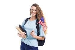 Smiling student woman in glasses with backpack holds books, notebooks and flag USA while on white studio background