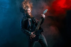 Emotional expression rock guitar player with long hair and beard plays on the black background. Smoke background. Studio shot. 