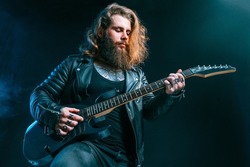Guitar player. Rockstar bearded man with long hair plays on electric guitar isolated on smoke black background. Studio shot 