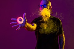 young man reaches for ring of smoke with his hand while blowing smoke. color filters. Vaping concept. Studio shot 