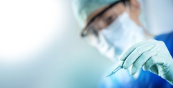 close up of the surgeon's hand holding a scalpel and blurred female doctor's face in the background with copy space, concept of surgical operations, hospitals and clinic staff