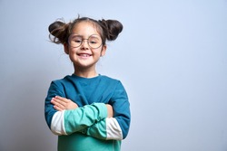 Portrait of cute swarthy caucasian little girl with glasses, arms crossed and funny hairstyle, beautiful happy child smiling and laughing looking at camera isolated in studio