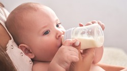 Mom feeds her happy child son baby milk powder, baby bottle