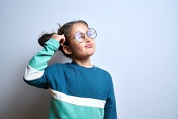 Funny little girl in glasses scratching her head doubts, makes decision isolated on yellow studio background