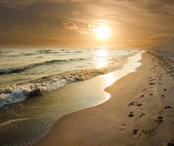 golden sunset on the sea shore and footprints in the sand