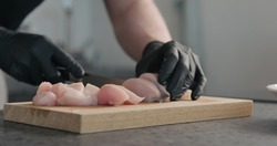 Man hands in black gloves cutting chicken fillet on oak board
