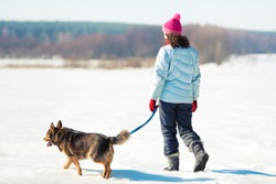 Young woman with her dog walking on the snowy field
