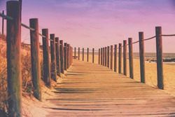 Wooden walkway on the sandy seashore in the magical light of the sunset. Beautiful seascape in the evening