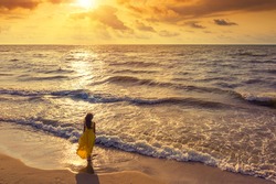 Seascape during golden sunrise with beautiful sky. Woman on the beach. Young happy woman in a yellow fluttering dress walks along seashore. The girl looks at the magical sunrise.  Above view. Top view