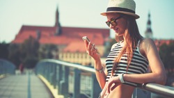 Woman using smartphone in the European city. Hipster girl browsing Internet on a phone, texting and communicating outdoors. Travel concept
