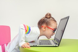 beautiful cute little girl looking at laptop screen very closely with open mouth. Shocked or surprised little girl on the internet in laptop computer on table.