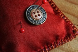 DECORATIVE BUTTON PINNED TO A PIN CUSHION WITH RED AND GREEN GLASS HEAD PINS