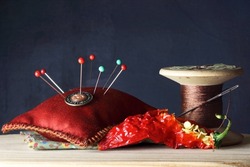 OLD WOODEN COTTON THREAD REEL AND RED PIN CUSHION, BUTTON AND GLASS HEAD PINS WITH SHRIVELLED DMAMGED RED CHILI