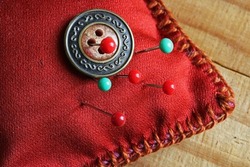 DECORATIVE BUTTON PINNED TO A RED PIN CUSHION WITH RED AND GREEN GLASS HEAD PINS