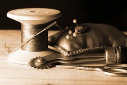 SEPIA IMAGE OF VINTAGE COTTON REEL AND PIN CUSHION
