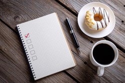 Book with blank checklist with coffee and donuts on rustic wooden table