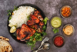 Tandoori chicken wings with spicy pilau rice, lime and traditional assortment of sauces on rustic table, top view