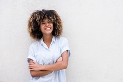 Horizontal portrait smiling young african american teen girl with curly hair and arms crossed by white background