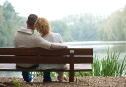 Rear view of a happy couple sitting together on bench outdoors