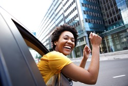 Portrait of cheerful young african woman looking out the car window with her arms raised