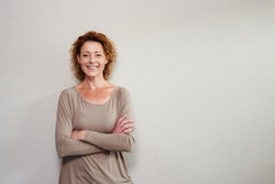 Portrait of older woman smiling with arms crossed by wall