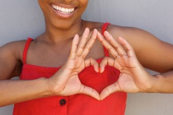 Close up portrait of young woman smiling with heart shape hand sign 
