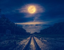 Railroad tracks through the woods at night. Beautiful dark sky and full moon above silhouettes of trees and railway. Serenity nature background. Outdoor at nighttime. The moon taken with my own camera