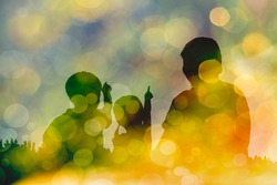 Silhouette of mother and two kids. Little children point to sky. Twinkling lights vivid blurred bokeh abstract in yellow background. Friendly family.