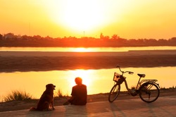 Silhouetted man with a dog watching sunset at Mekong river waterfront, Vientiane, Laos, Southeast Asia