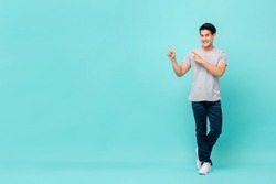 Confident smiling young Asian man pointing hands to copy space aside studio shot isolated on light blue bakground