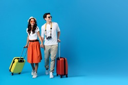Happy young couple being ready to go for their holidays with colorful suitcases isolated on blue background with copy space