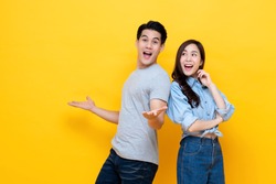 Attractive smiling young Asian couple being happy and amazed isolated on yellow studio background