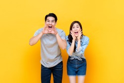Young lovely asian couple yelling with hands cup around mouths isolated on yellow studio background