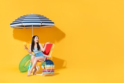 Surprised beautiful young Asian woman sitting on beach chair doing an open palm gesture isolated on bright yellow studio background with copy space
