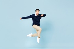 Young handsome Asian man smiling and jumping in mid-air on light blue studio background