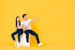 Happy surprised attractive young Asian couple pointing and looking at blank space beside in yellow isolated stuidio background