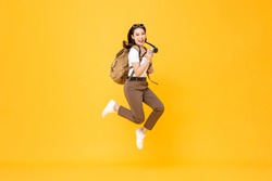 Young pretty Asian woman tourist backpacker smiling and jumping with camera in hand isolated on yellow background