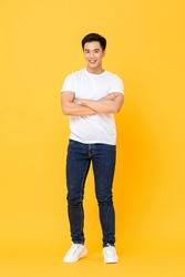 Smiling young handsome Asian man standing with arms crossed gesture isolated on yellow studio background
