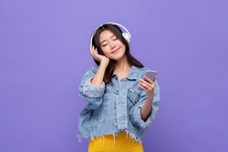 Happy Asian girl wearing headphones listening to music from mobile phone relaxing with eyes closed on isolated purple studio background