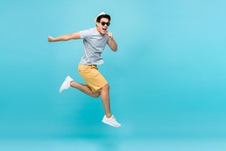 Energetic happy young Asian man jumping studio shot isolated in light blue background