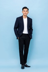 Full length portrait of happy smiling young handsome southeast Asian businessman standing on light blue studio background