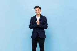 Smiling young handsome southeast Asian man clapping hands impressively in light blue studio isolated background