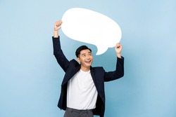 Young happy handsome smiling Asian man holding empty speech bubble in light blue isolated studio background