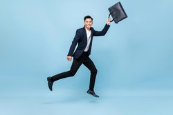 Portrait of smiling young handsome Asian male office worker running in mid-air holding bag in light blue isolated studio background