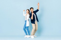 Full length portrait of cheerful Asian couple standing back to back smiling and clenching fists in light blue isolated studio background