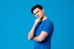 Young curious handsome Caucasian man thinking with hand touching chin in  isolated studio blue background
