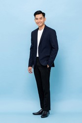 Full length portrait of young handsome southeast Asian millenial businessman looking at camera on light blue studio background