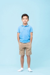 Full body self assured child in casual clothes and socks holding hands in pockets and looking at camera against blue background